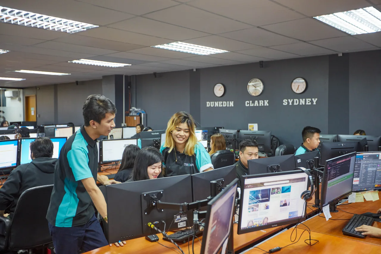 List Building & Database Management outsourcing in the Philippines — colleagues collaborating around a desktop computer beneath office wall clocks